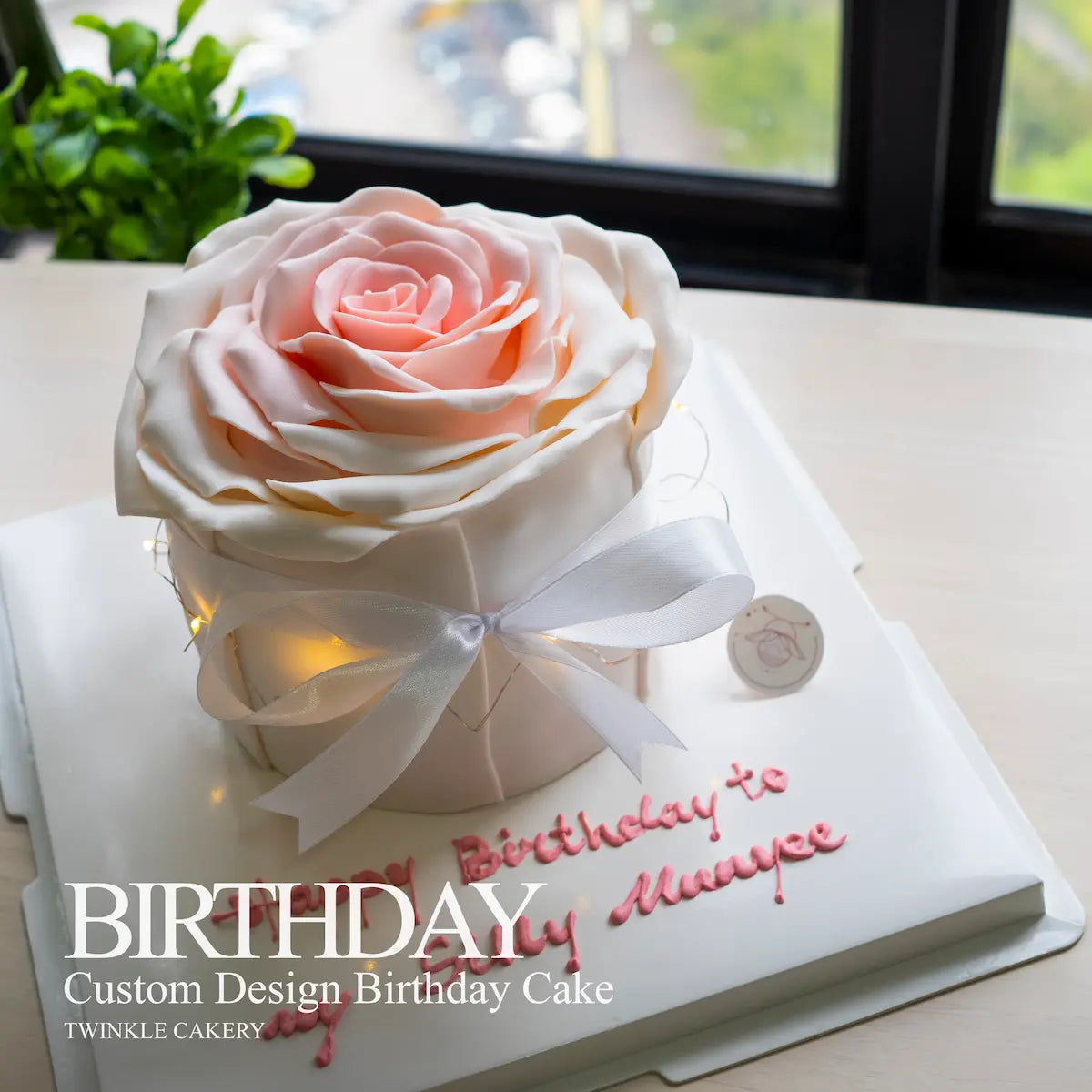 Custom design birthday cake with a large pink rose and 'Birthday' text, featuring Twinkle Cakery branding.