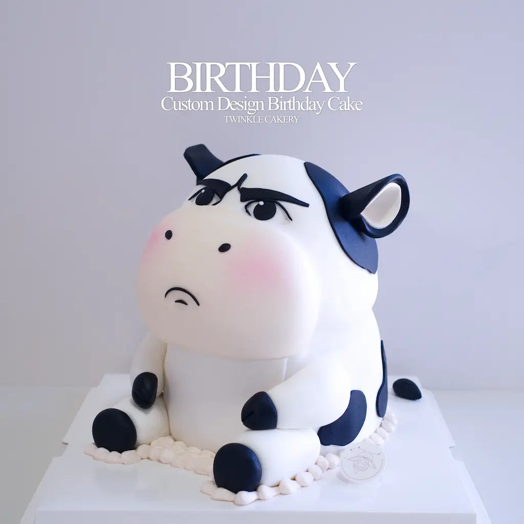 A custom 3D cartoon cow birthday cake with a grumpy expression, decorated in white and navy blue with pink cheeks, with edible fondant details by Twinkle Cakery KL and Selangor

