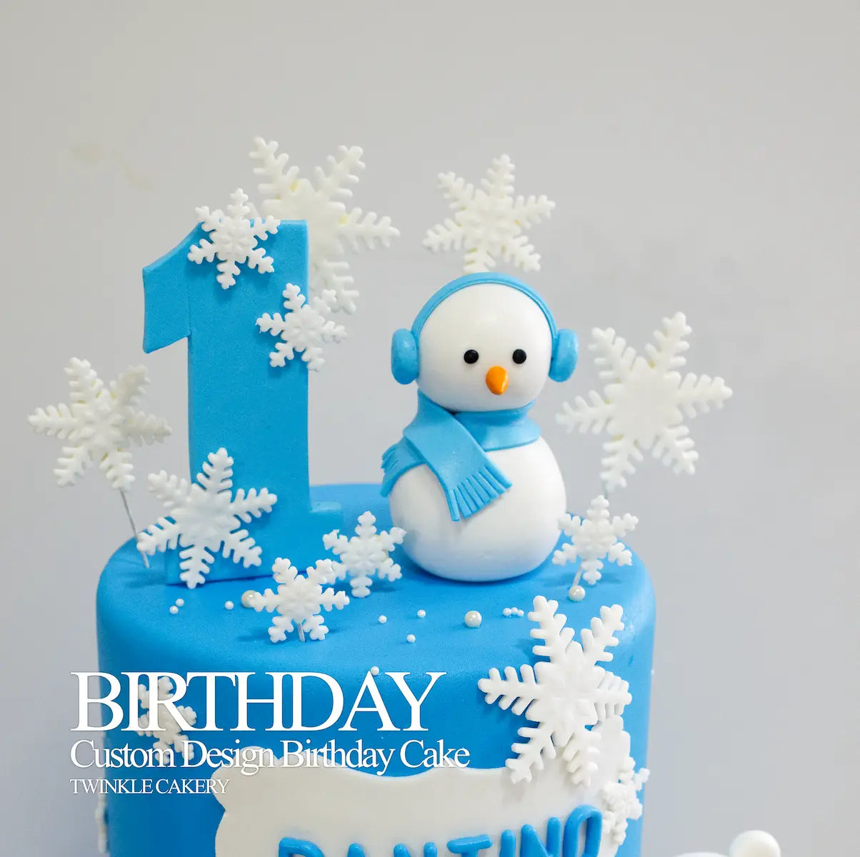 Close-up of a custom number one cake topper on a blue Winter Wonderland birthday cake.