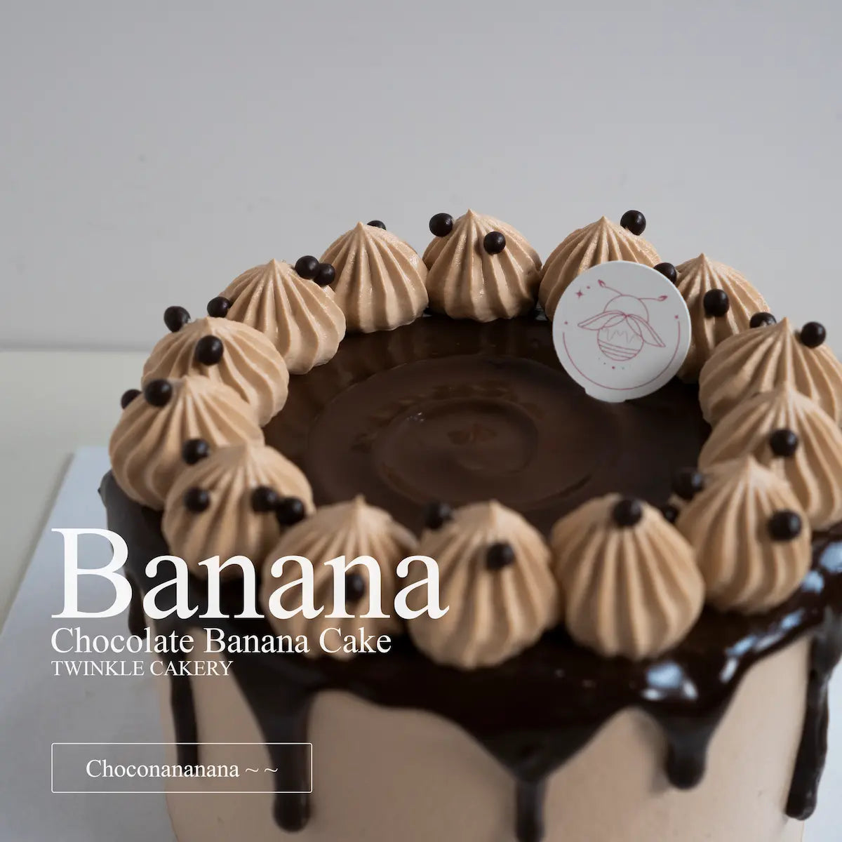 Artisan baker applying a rich chocolate ganache drip onto a fresh cream chocolate banana cake in the kitchen.